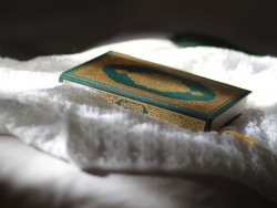 Bildet viser en koranbok som ligger på et hvitt stoff.