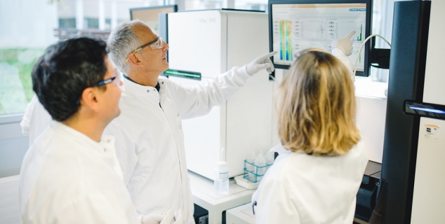 Foto av tre personer med hvit frakk i et laboratorium