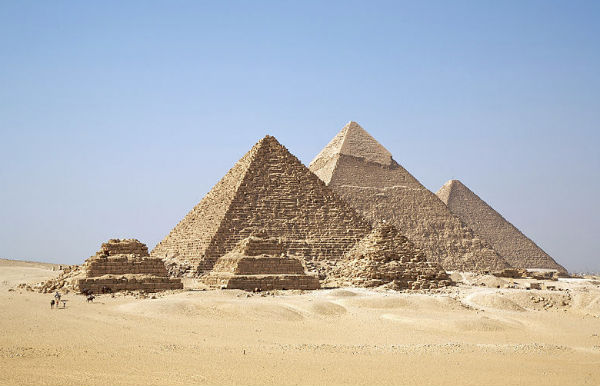 Bilde i farger. Flere pyramider. Rundt er det gul sand og blå himmel.