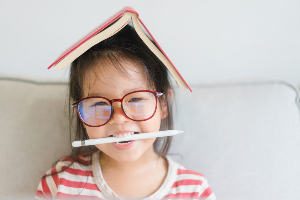 en jente med en bok på hodet og en penn i munnen