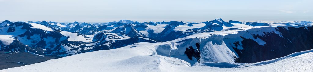 Oversiktsbilde av et fjellområde med mange spisse fjelltopper. Det er snø på fjellene.