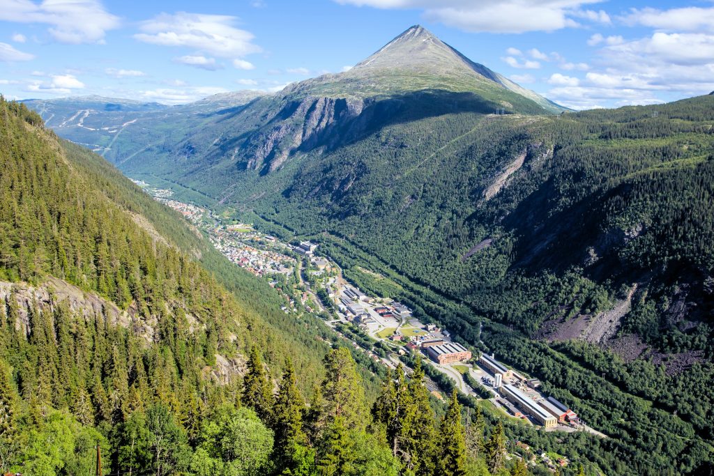 Oversiktsbilde av et landskap med en dyp dal. Nede i dalen ligger en lang og smal by. Øverst i bildet er en kjegleformet fjelltopp.