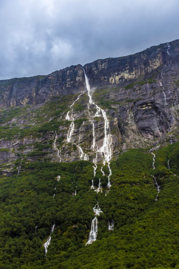 Fotografi av en fjellside med en smal foss som deler seg i mange enda smalere fosser som strømmer nedover fjellsiden.