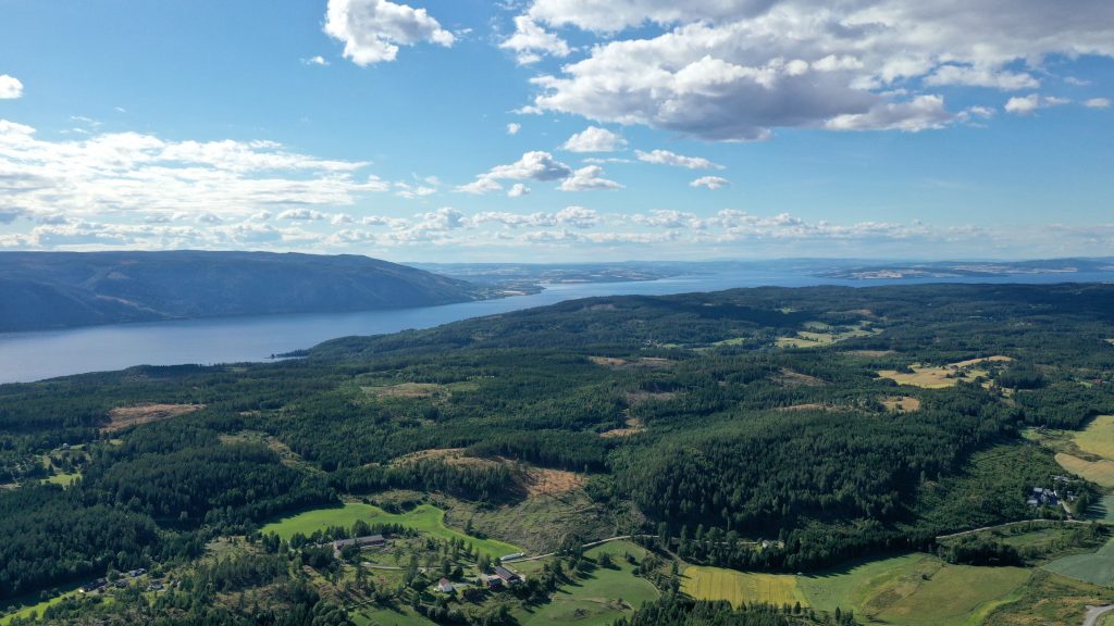 Oversiktsbilde av landskap med skog og åkere. Gjennom landskapet strekke det seg et lang og smal innsjo.