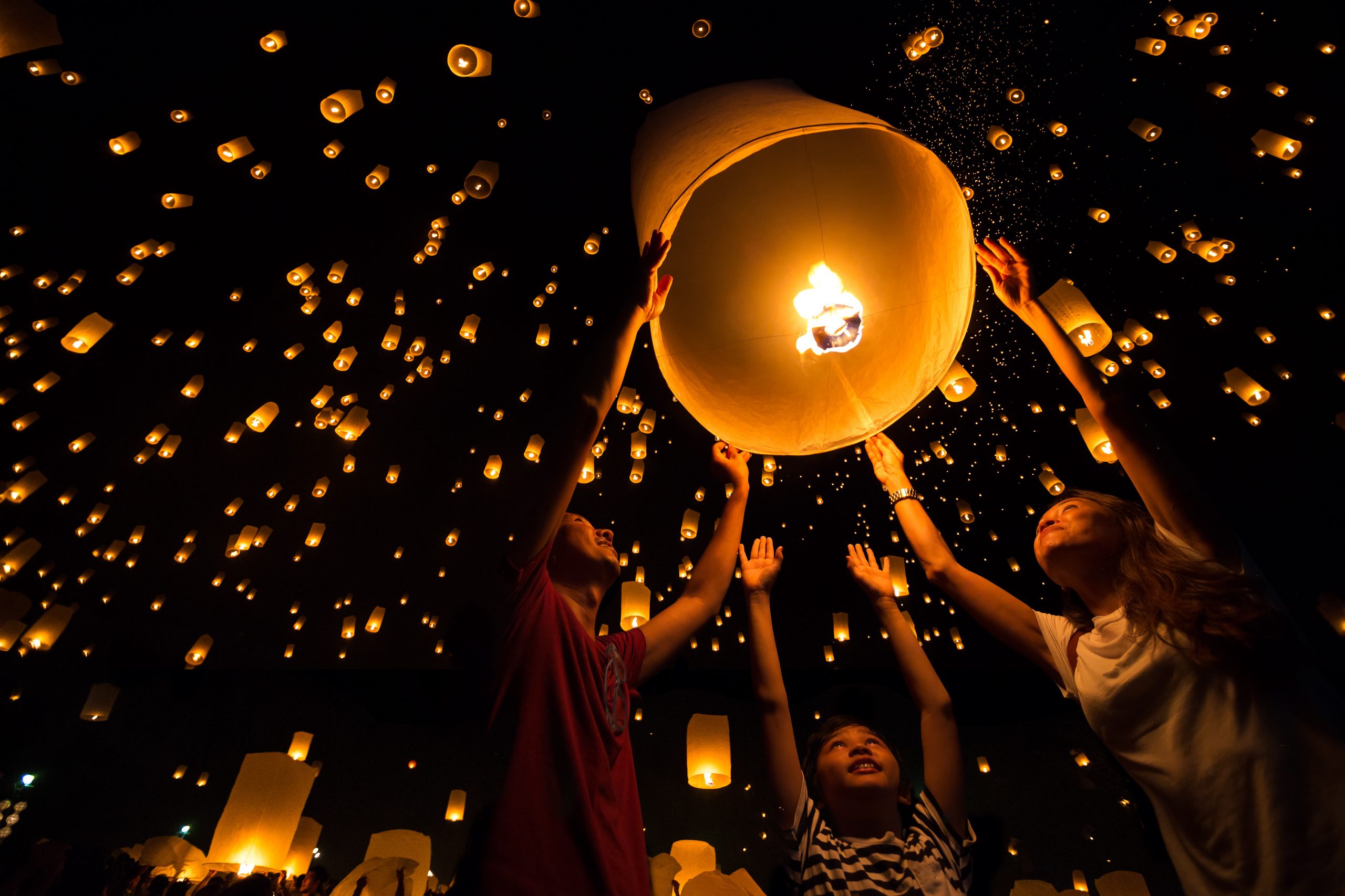 Bilde av tre personer som sender opp en lanterne på himmelen for å feire Buddha i høytiden Vesak