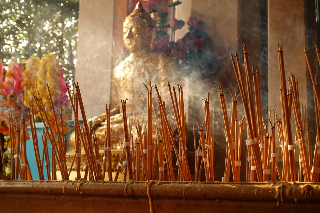 Bilde av et buddhistisk alter. Det er tent mange pinner med røkelse og du ser røyken spre seg.