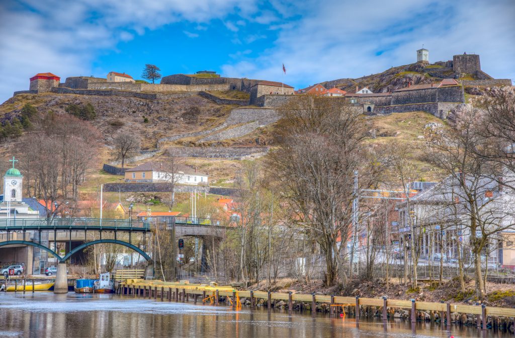 Fotografi av en gammel festning som ligger på en høyde over en by. Festningen er bygget av murstein