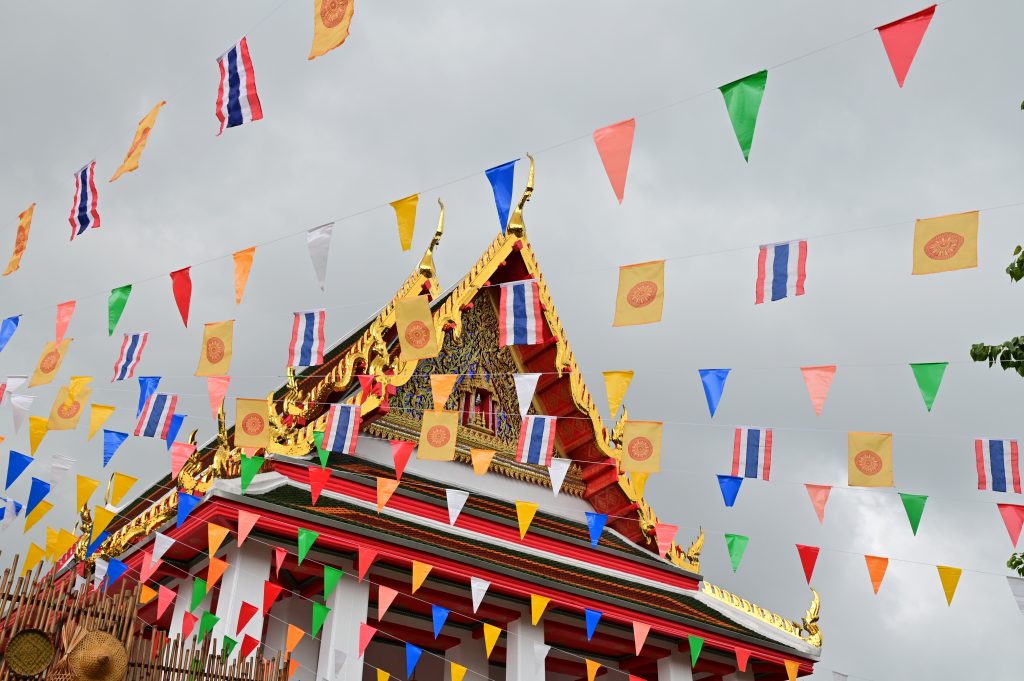 Bilde av mangle små buddhistiske flagg som henger på en mange snorer. I bakgrunnen skimtes et buddhistiske tempel. 