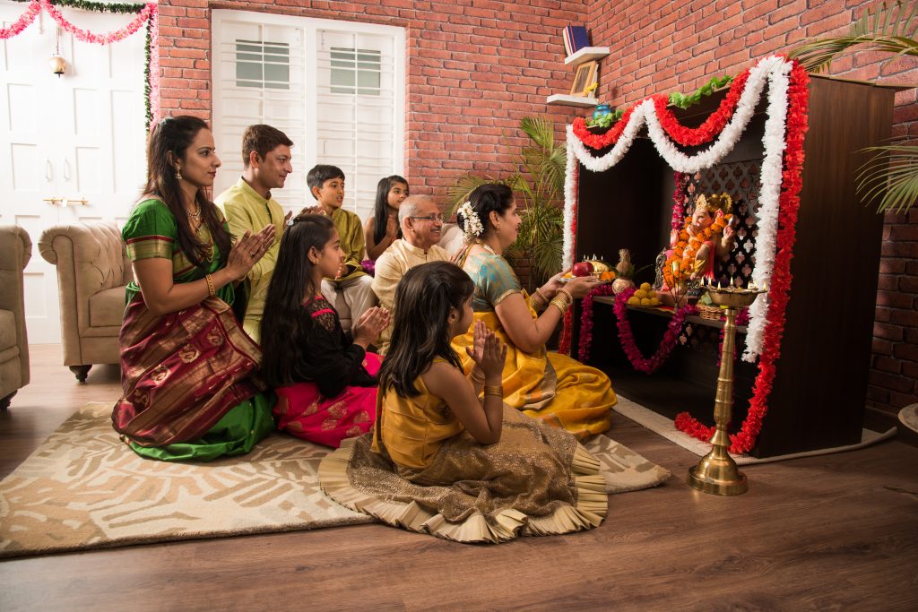 Bildet viser hele familien som tilber guden Ganesha via statuen som de har hjemme.  De setter frem frukt og blomster. 