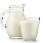 En glassmugge med hank og melk oppi, foran står et glass med melk