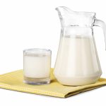 Et glass melk og en melkekanne på en rutet duk