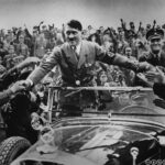 Sort-hvitt foto av en mann som står i en åpen bil. Det er tett i tett med folk rundt bilen.