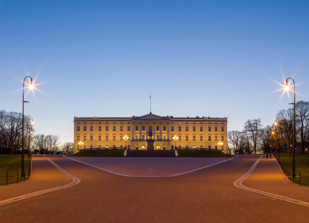 En stor gul bygning med mange vinduer på en åpen plass, bildet er tatt om kvelden.